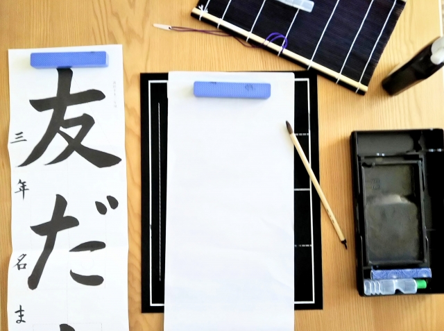 友だちと書かれた習字のお手本を左に置きこれから書き初めをしようとしているイメージ